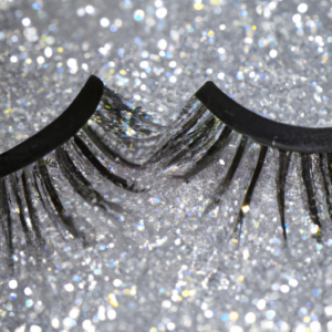 A close up of a pair of individual false eyelashes with a glittery background.