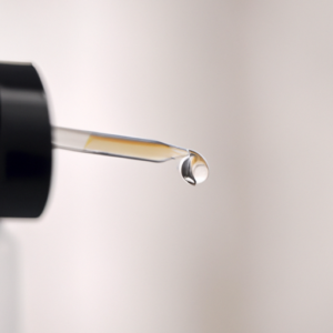 A close-up of a bottle of lash serum with a drop of the serum coming out of the nozzle.