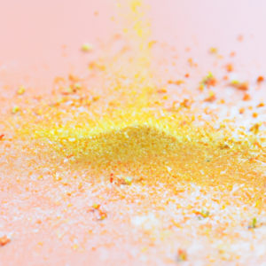 A close-up of a golden yellow powder being sprinkled onto a pale pink surface.